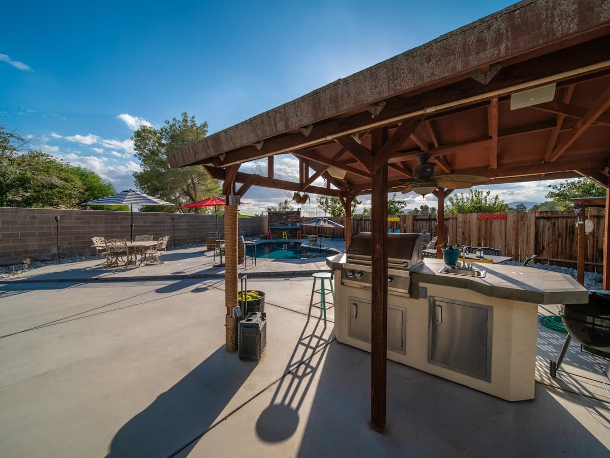 A covered concrete patio with a built-in grill station beside a pool deck
